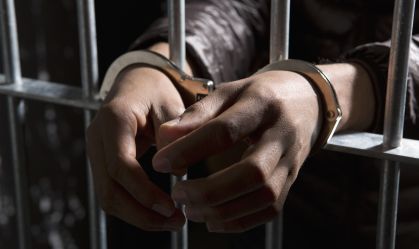 A prisoner behind bars with hands cuffed