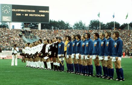 As seleções nacionais de futebol da Alemanha Oriental (de azul) e Ocidental (de branco) estão em fila para os hinos nacionais antes do início da partida na Copa do Mundo de 1974