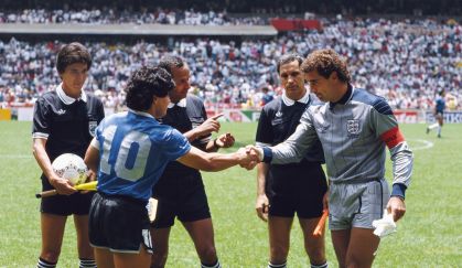 Diego Maradona (esq.) aperta a mão de Peter Shilton (dir.) sob os olhares do árbitro Ali Ben Nasser (centro) antes da partida entre Argentina e Inglaterra pelas quartas de final da Copa do Mundo de 1986, no México