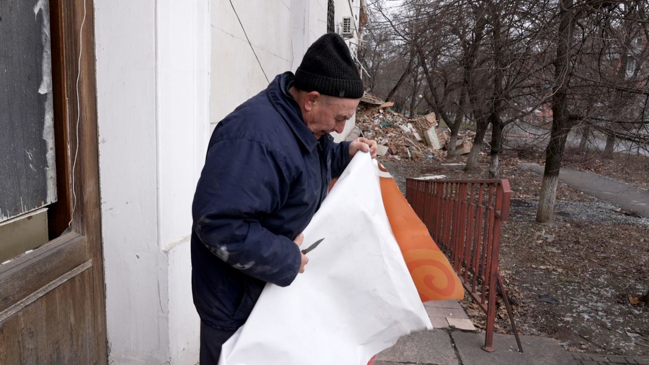 Anatoly corta um pedaço de plástico para cobrir suas janelas que foram destruídas pelos bombardeios em Kherson, na Ucrânia / Will Bonnett / CNN