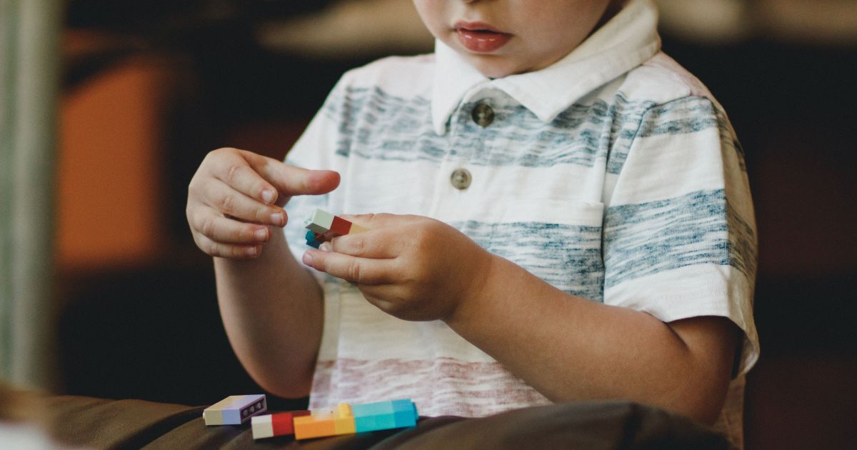 Criança brincando acompanhada por cuidador, ilustrando sinais precoces de autismo.