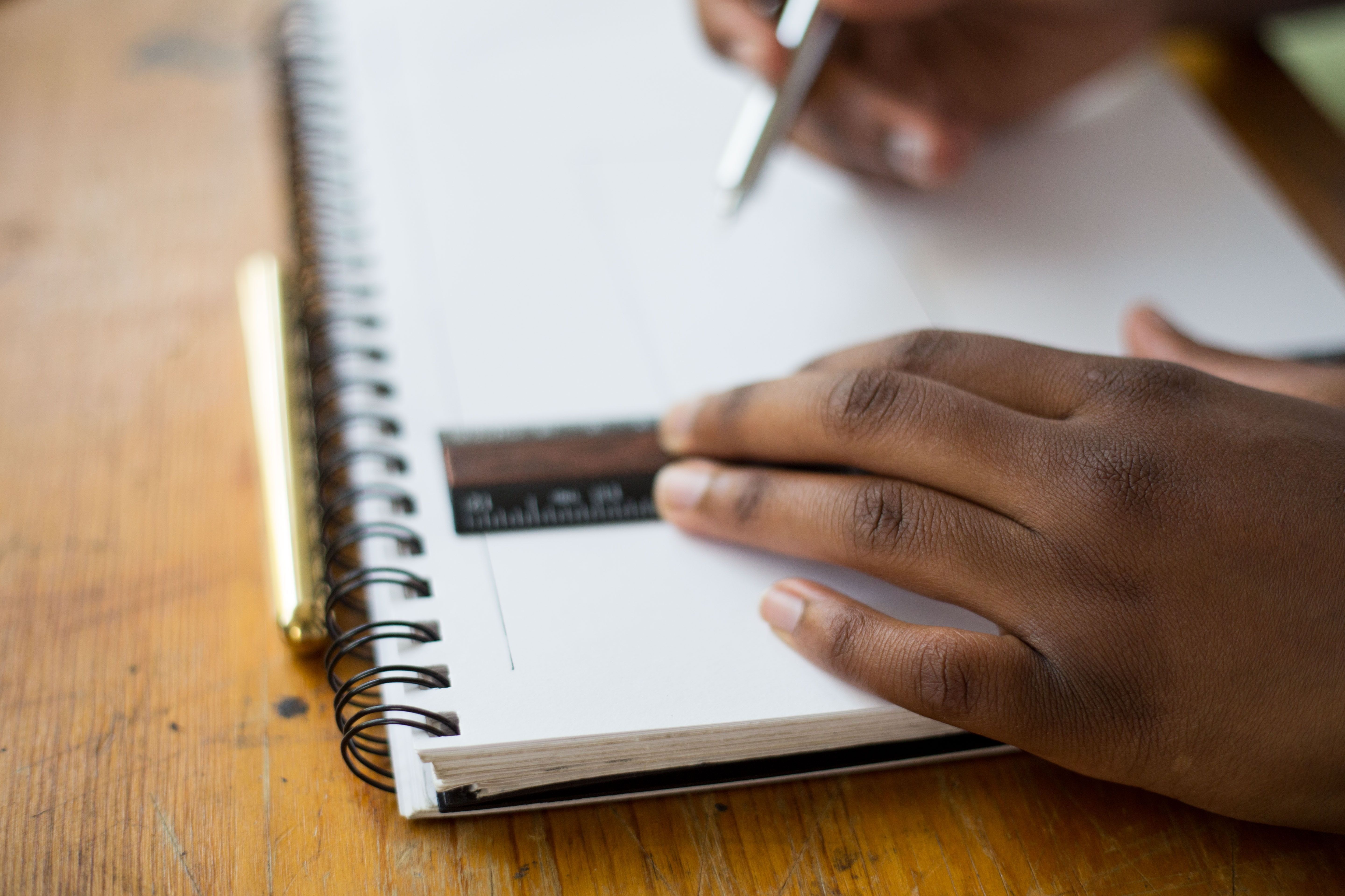 Mão negra de estudante com uma régua sobre um caderno