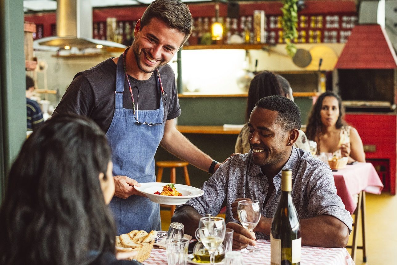 Cheerful male chef serving couple in restaurant and smiling