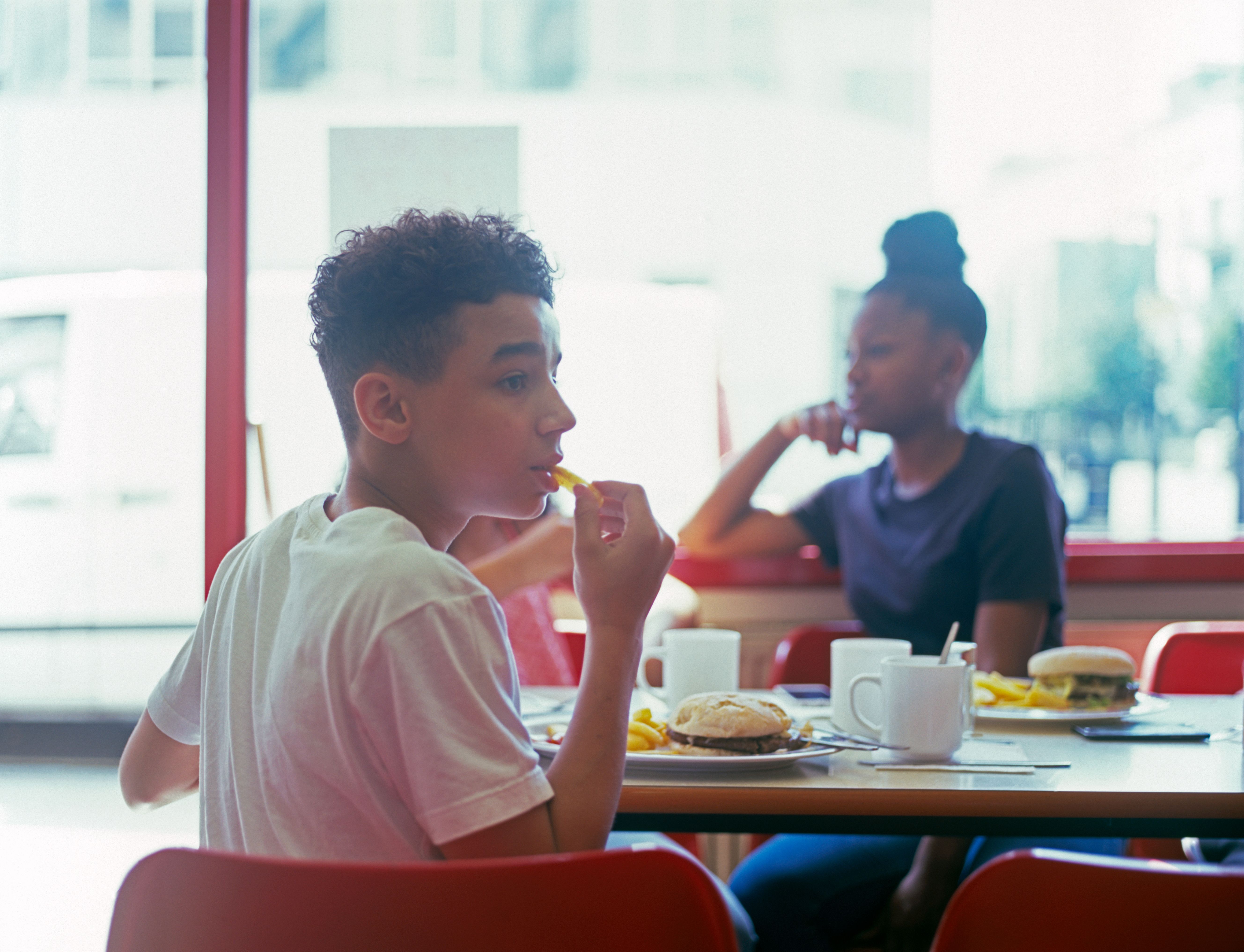 Teenage boy in cafe eating burger and chips