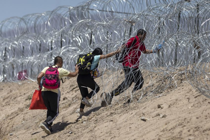 Imigrantes atravessam arame farpado em torno de um acampamento improvisado depois de cruzar a fronteira do México, em 11 de maio de 2023 em El Paso, Texas / Photo by John Moore/Getty Images