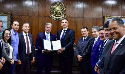 Acompanhado por diversos políticos, o presidente da Câmara, Arthur Lira (à esquerda), entrega uma pasta com o texto da reforma tributária a Rodrigo Pacheco (à direita), presidente do Senado