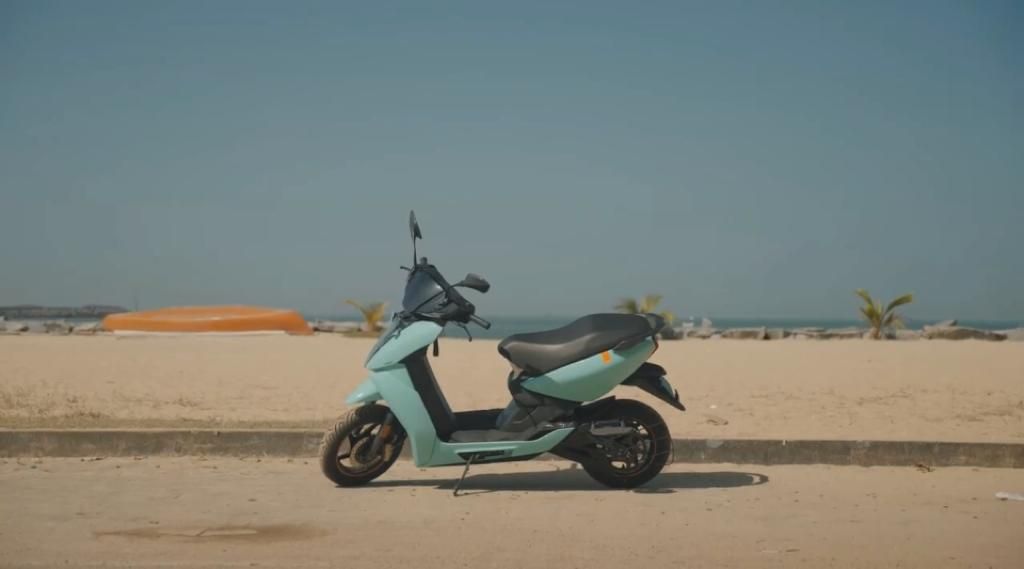 Scooter elétrica verde-água da Ather Energy em frente a areia da praia e céu azul