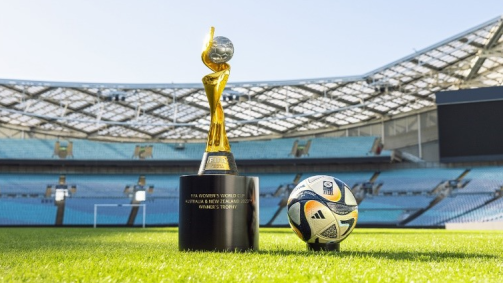 Em um estádio, é possível ver a taça da Copa ao lado da bola da final