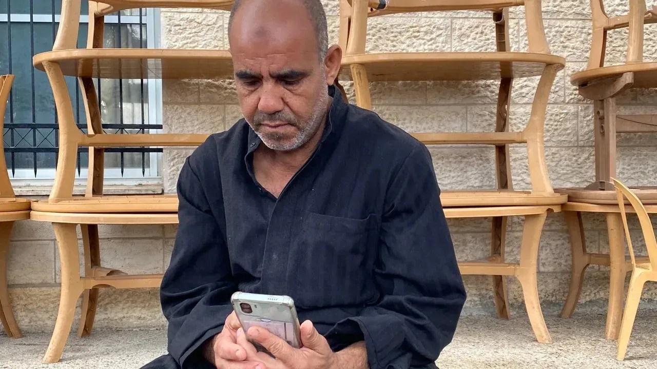 Marwan Saqer olha para seu telefone enquanto sua família tenta ligar para ele de Gaza, mas não consegue / Ivana Kottasova/CNN
