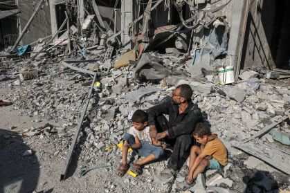 Família de palestinos sentados sobre os escombros de um dos prédios destruídos em ataque aéreo de Israel em Rafah, na Faixa de Gaza, em 12 de outubro de 2023.