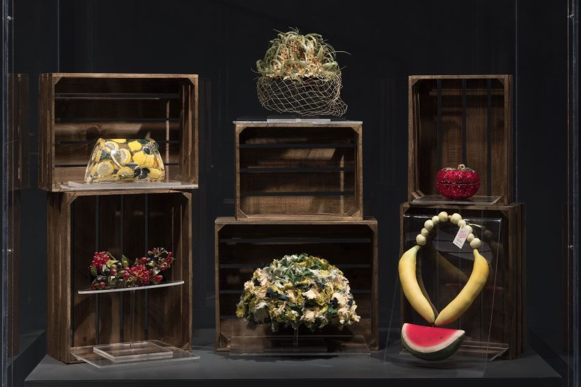 Exposição "Food & Fashion" apresenta acessórios, incluindo uma bolsa Lucite com estampa de limão (canto superior esquerdo) da artista Joyce Francis, um chapéu com espiga de milho (centro) do modista Benjamin B. Green-Field e um colar grosso lembrando melancia, banana e uva (canto inferior direito) / The Museum at FIT/Divulgação
