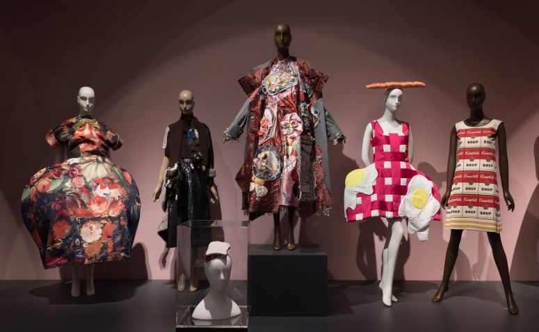 As peças incluídas na exposição "Feeding the Eye" incluem um vestido escultural da coleção primavera-verão 2018 da Comme des Garçons (extrema esquerda), um chapéu sanduíche PB&J desenhado por Stephen Jones (centro em primeiro plano) e o papel "Souper Dress" desenhado por Campbell's Soup Company por volta de 1966 (extrema direita) / The Museum at FIT/Divulgação