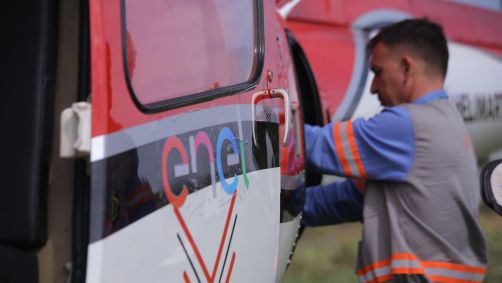 Funcionário da Enel ao lado de helicóptero com o o logo da empresa.