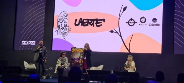 Laerte Coutinho em painel da CCXP23 Unlock, segurando um poster do filme "Overman"