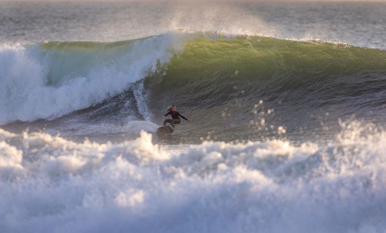 Jovem surfista faz uma curva enquanto surfa uma grande onda ao pôr do sol em Newport Beach / Los Angeles Times via Getty Images