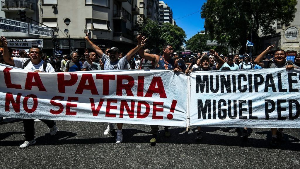 Manifestantes seguram uma faixa que diz "O país não está à venda" e gritam slogans em frente aos Congressos Nacionais durante uma greve nacional contra as políticas do presidente Javier Milei convocada pelo sindicato dos trabalhadores CGT em 24 de janeiro, 2024 em Buenos Aires, Argentina