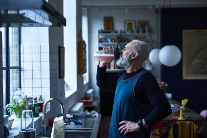 Homem idoso tomando suplemento proteico em sua cozinha