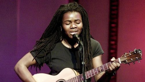 Tracy Chapman cantando no microfone segurando um violão