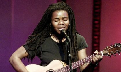 Tracy Chapman cantando no microfone segurando um violão
