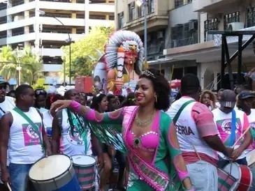 passista samba durante um bloco pelas ruas do RJ. A fundo, uma alegoria com o dorso de um indígena. Ao lado, a bateria.