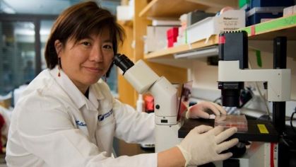 Médica Catherine Wu sorrindo para uma foto com um microscópio em sua frente