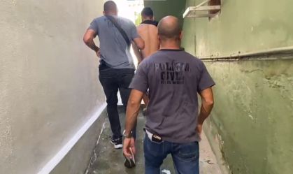 Dois policiais civis acompanham o criminoso José Roberto Muniz de Sousa, o Ret, que está sem camisa
