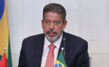 Arthur Lira, sentado e de terno, com uma gravata vermelha, olha para frente enquanto fala
