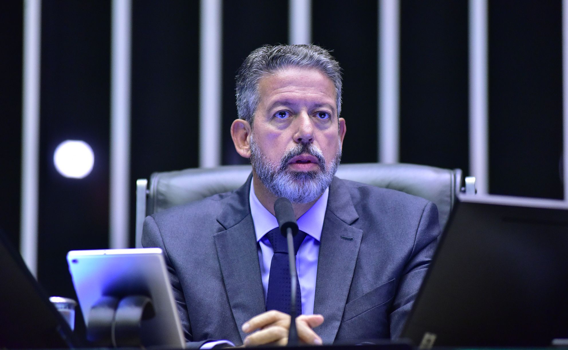 Arthur Lira sentado em uma cadeira de couro olha para frente enquanto fala ao microfone