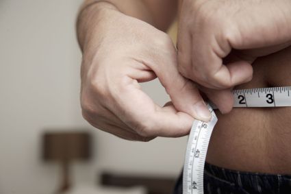 Homem medindo a circunferência da cintura com uma fita métrica