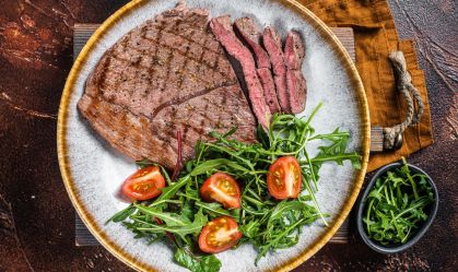 Diner with grilled beef veal meat steaks and vegetable salad. Dark background. Top view
