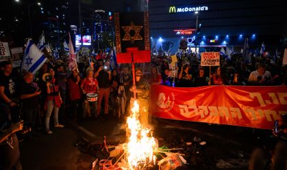 Mulher com uniforme falso da FDI e manifestantes acendem fogueira pedindo libertação de reféns mantidos na Faixa de Gaza e contra o primeiro-ministro israelense Benjamin Netanyahu em 30 de março de 2024 em Tel Aviv