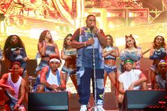 Vocalista segurando o microfone rodeado com seu balé