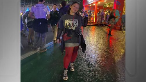 Jovem fazendo sinal da paz com os dedos e vestindo saia, camiseta de banda e um casaco amarrado