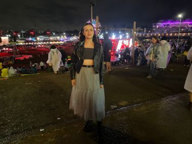 Mulher segura a saia mostrando a roupa com cenário do festival e roda gigante