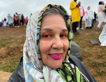 Senhora com pano na cabeça sorrindo e mostrando maquiagem