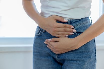 Mulher veste calça jeans e blusa branca e coloca as mãos sobre a região do útero, com cólica menstrual