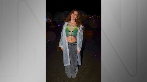 Cantora Marina Sena olhando para a foto com calça jeans acinzentada, blusa verde e cardigan transparente