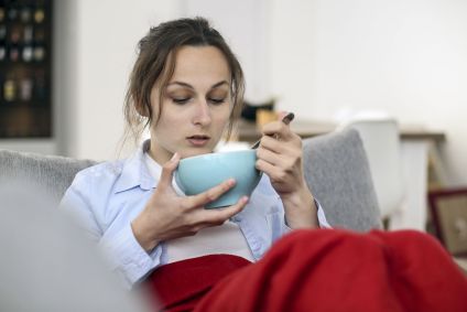 Mulher sentada no sofá tomando sopa