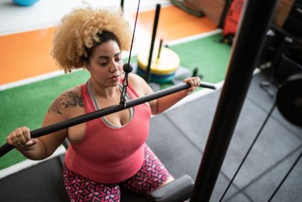 Jovem mulher puxando uma barra em exercício na academia