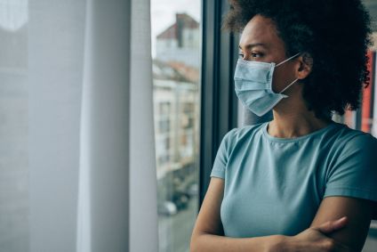 Mulher usa máscara facial e olha para a janela do apartamento