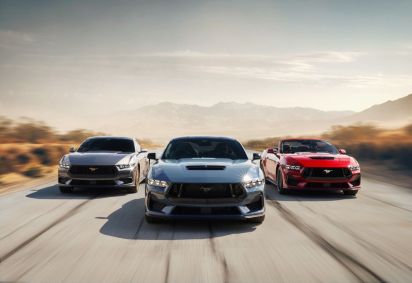 Trio de carros esportivos Ford Mustang, nas cores cinza, azul e vermelho, é visto na pista