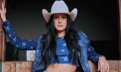 Foto da cantora Ana Castela usando um chapéu branco e roupa jeans