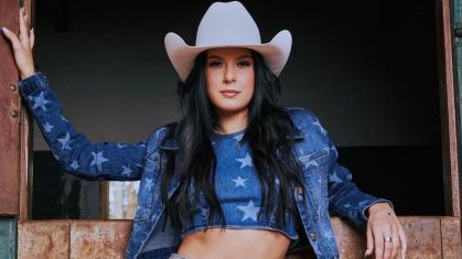 Foto da cantora Ana Castela usando um chapéu branco e roupa jeans