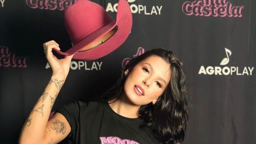Cantora Ana Castela segurando um chapéu rosa