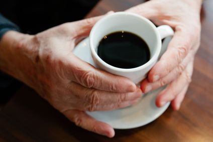 Idoso com as mãos segurando uma xícara de café