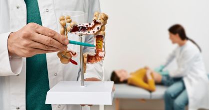 Em primeiro plano, médico mostra um modelo em 3D de intestino; em segundo plano, médica examina o abdômen de uma paciente