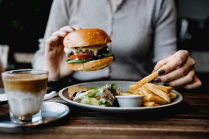 Recorte de foto de mulher segurando um hamburguer e pegando uma batata frita em um prato