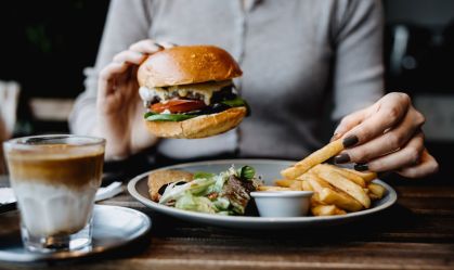 Recorte de foto de mulher segurando um hamburguer e pegando uma batata frita em um prato