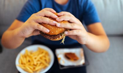 Recorte de imagem de adolescente segurando um hamburguer com as mãos, com um prato de batatas fritas no colo