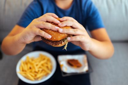 Recorte de imagem de adolescente segurando um hamburguer com as mãos, com um prato de batatas fritas no colo